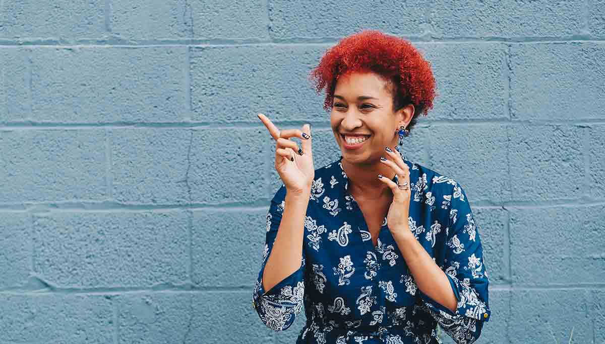 Black woman laughing pointing and standing in front of a blue concrete wall