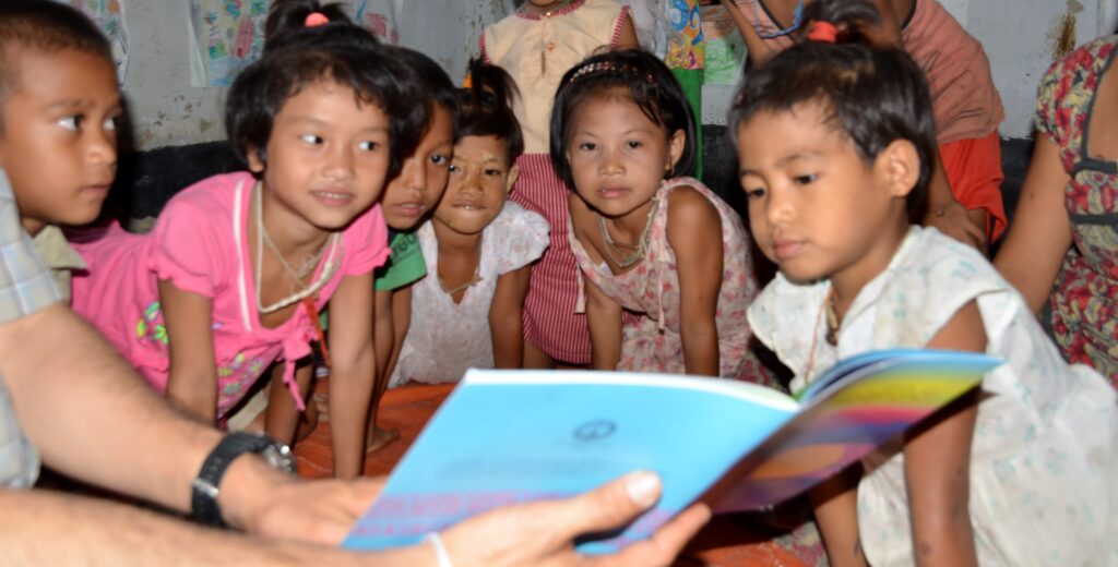 Children in Bangladesh crowd around a book in their native language.