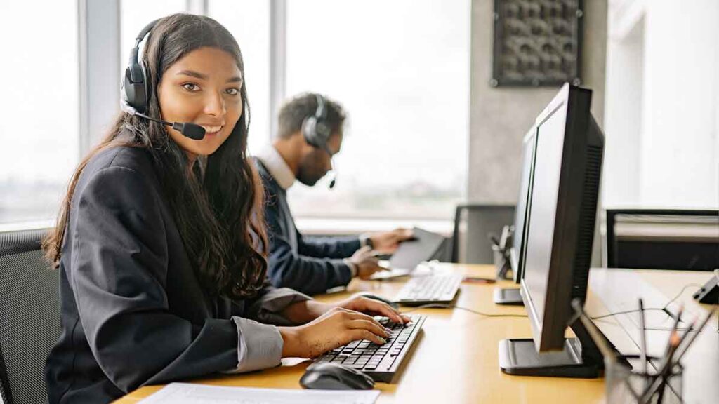 Female call center agent wearing headset and sitting next to her male colleague at her workstation. She is happy because she just used telephone interpretation services.