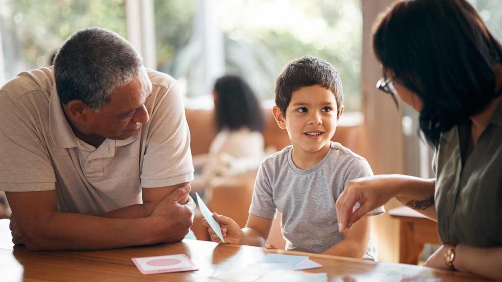 A young student plays a flashcard game with a parent and a teacher.