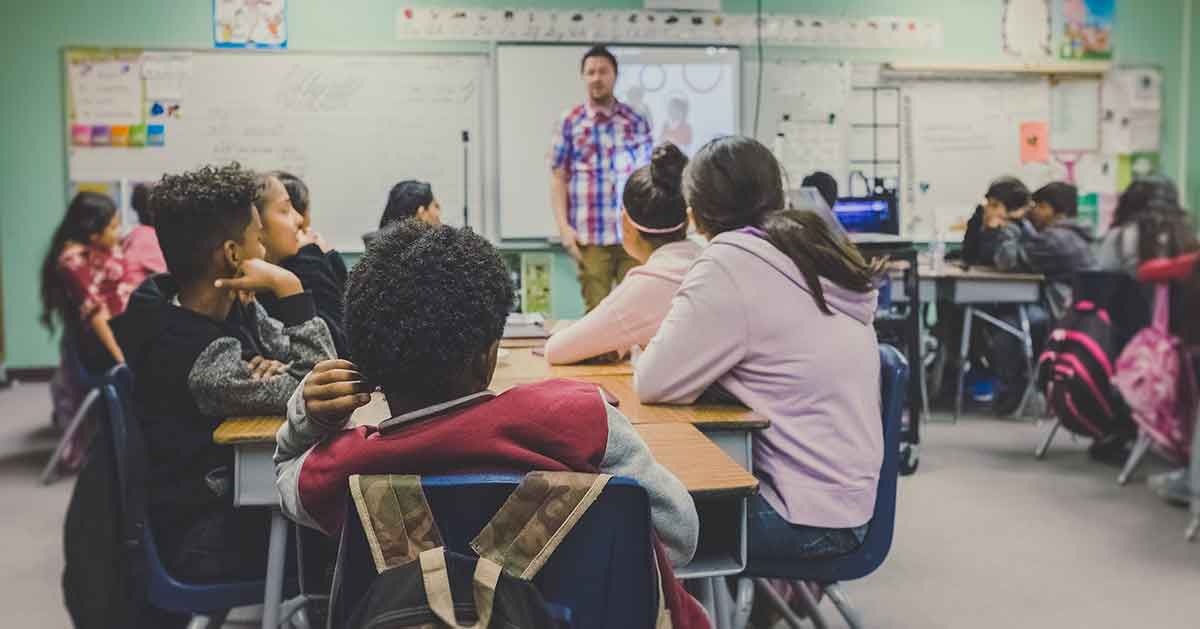 A classroom full of students sit engaged listening to their teacher. Interpreters can help parents understand what is happening in their child's education.