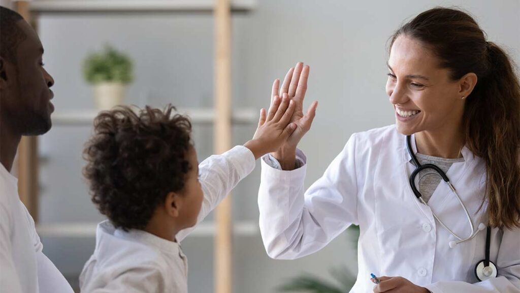 A parent holds their child as they high five a kind doctor.