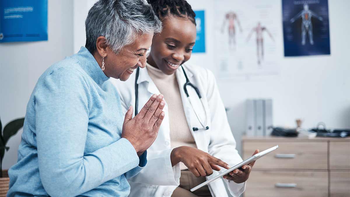 A doctor and patient smile as they work with a video interpreter on a tablet.