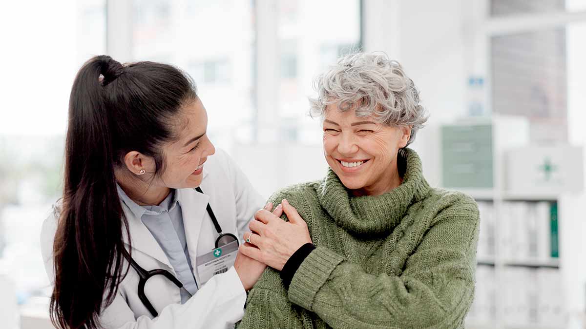 A happy doctor clasps the hand of a widely smiling patient.