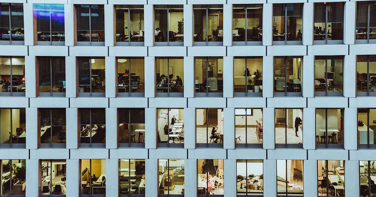 Many windows on side of office building showing people work