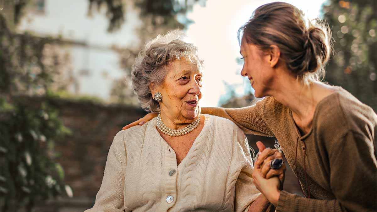 A grandmother and grandchild sit on a courtyard bench on a peaceful day and hold hands as they talk.