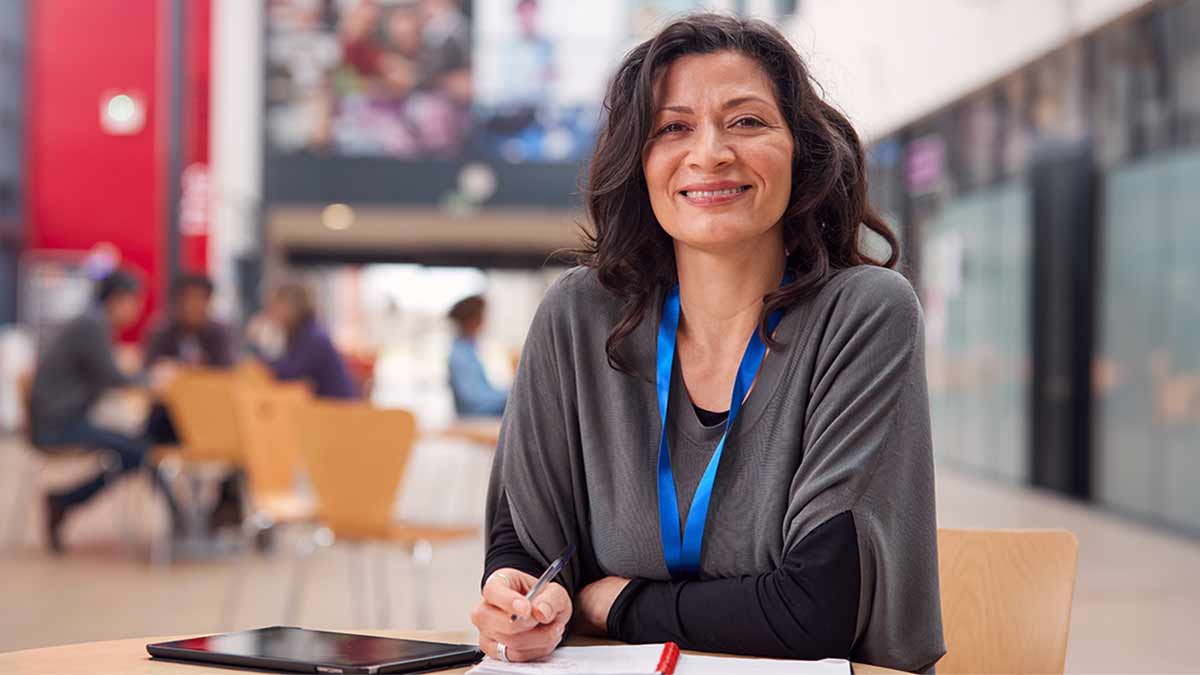 A Spanish interpreter smiles at the camera from their desk with a tablet beside them and a pen and notebook in hand.