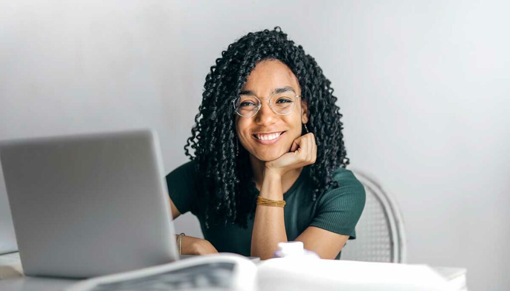 A Black female freelance interpreter sits in front of her. She's smiling with her chin resting on her hand.