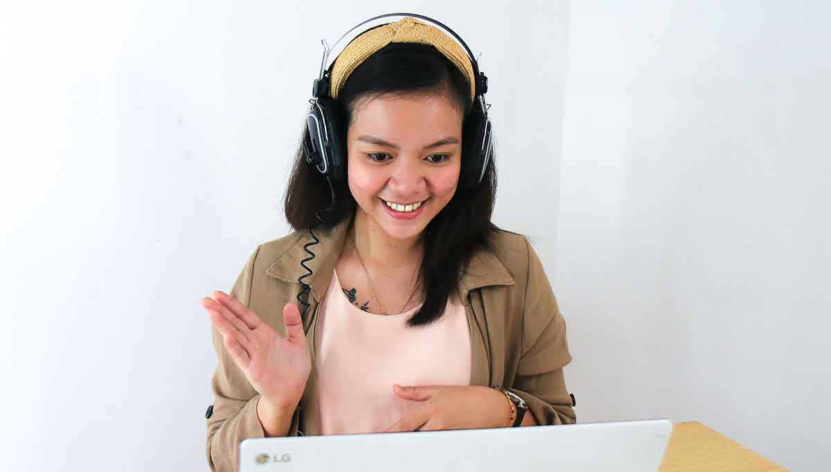 Female interpreter wearing a headset smiling and introducing herself at the start of a video interpreting session looking at the laptop in front of her.