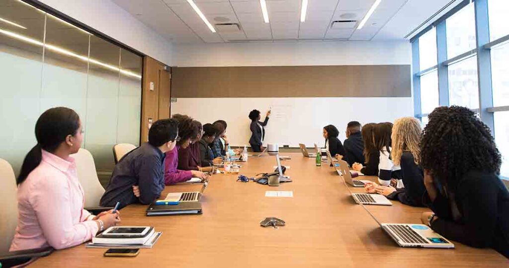 Female language access coordinator presenting to her staff sitting around a large table. She is answering their questions about language access.