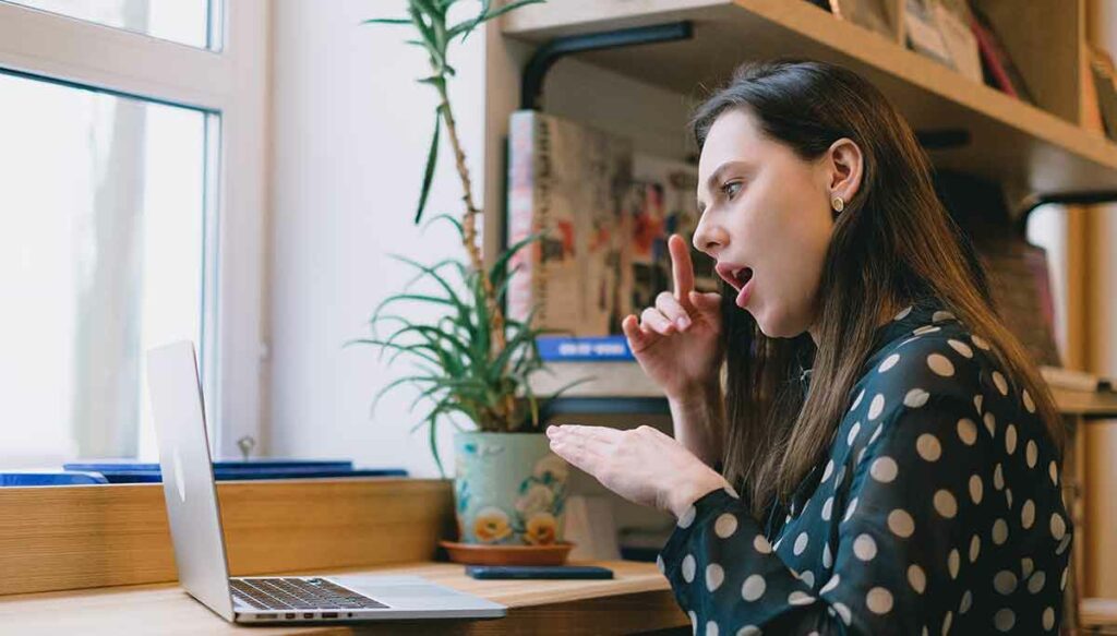 Female sitting at a table using American Sign Language over a video remote interpreting platform to communicate with another person.