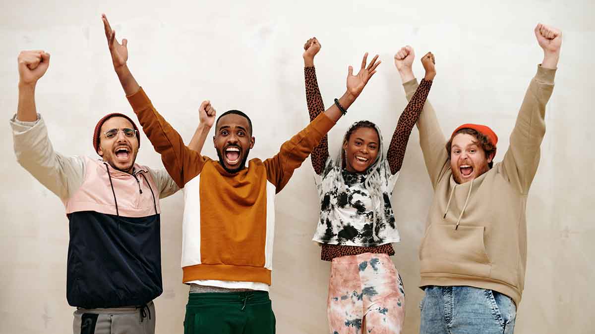 Three men and one women are raising their hands in the air with excitement. They all have their mouths open like they're screaming "Yay!"