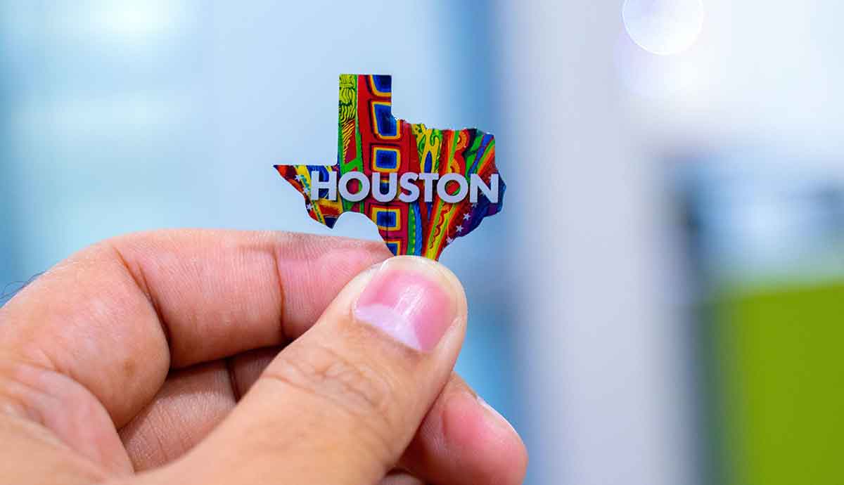 Close-up of a hand holding a pin in the shape of Texas. The pin is colorful and has Houston written on it.