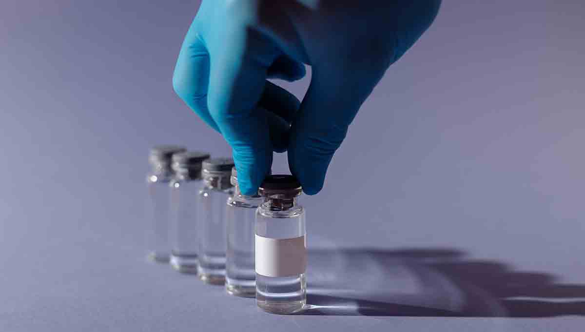 Gloved hand lining up five vials of COVID-19 vaccine.