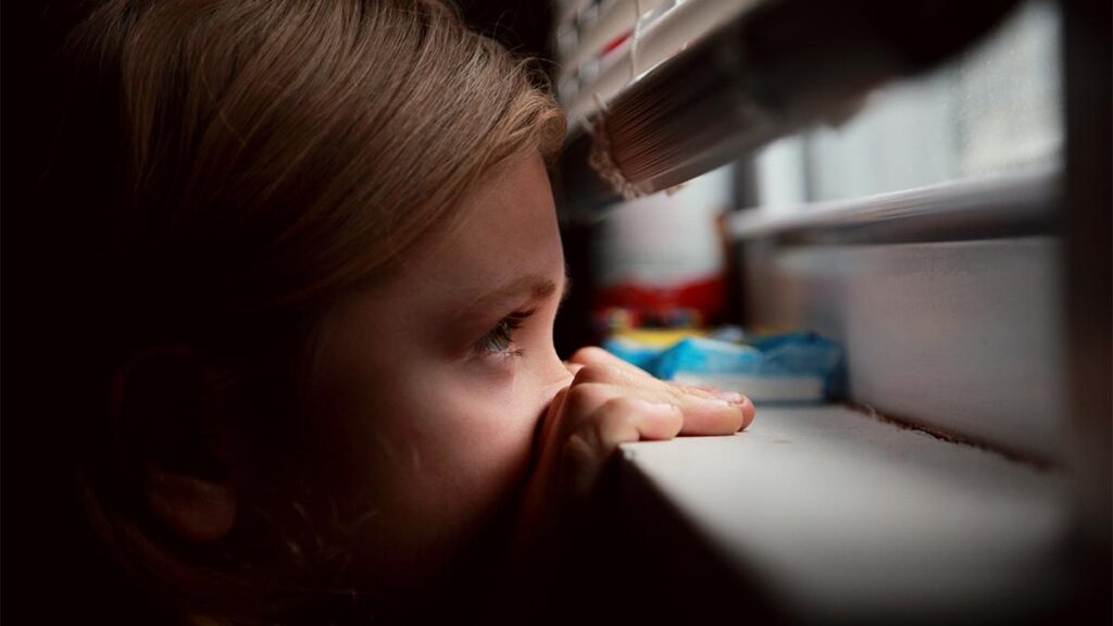 A hiding child peeks through a window.