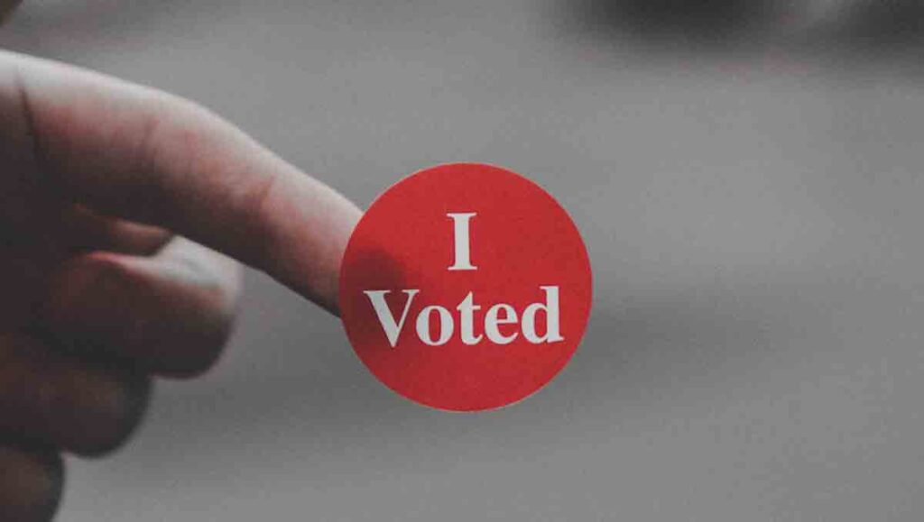 Hand holding red "I voted" sticker