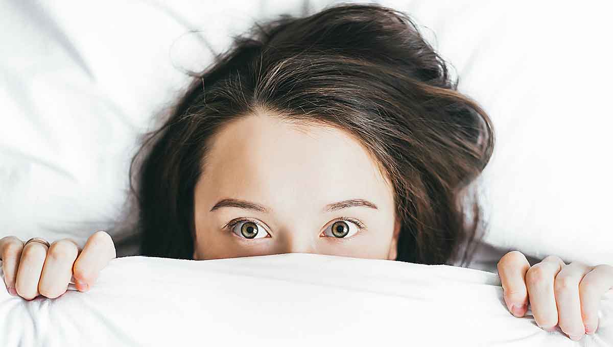 A few interpreter with lying awake in her bed from a nightmare. The covers are pulled up over her nose.