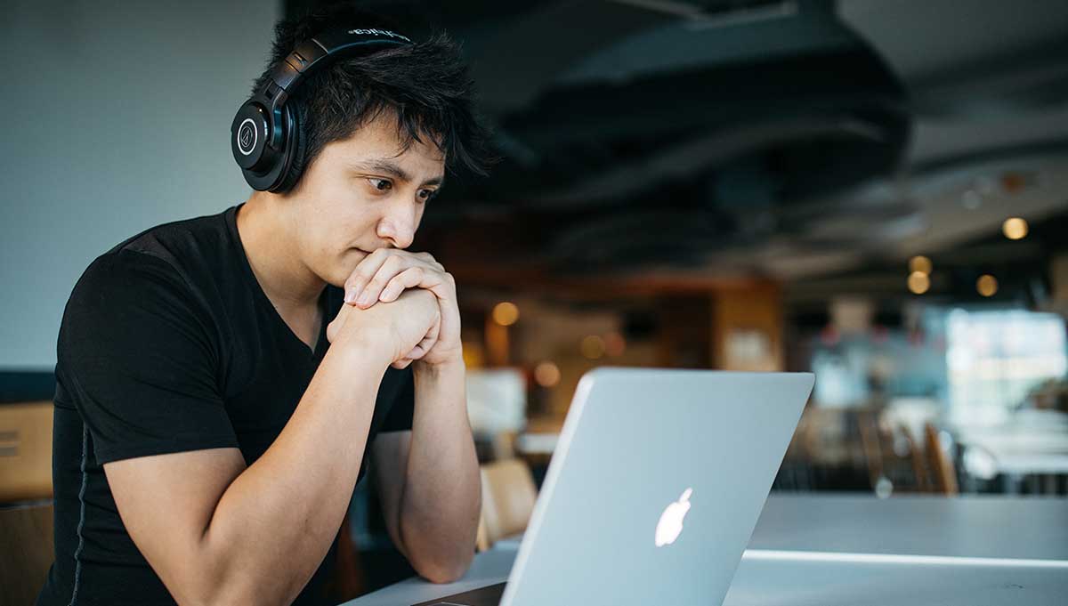 Male wearing headphones stares at his laptop while studying for his medical interpreter certification