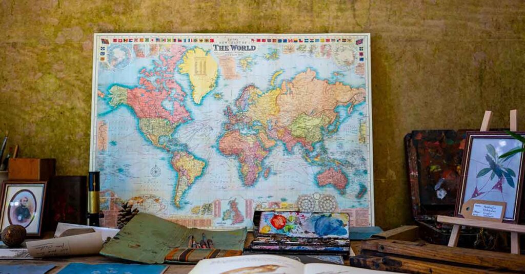 World map leaning against a wall surrounded by paint, papers, a picture, and a small easel