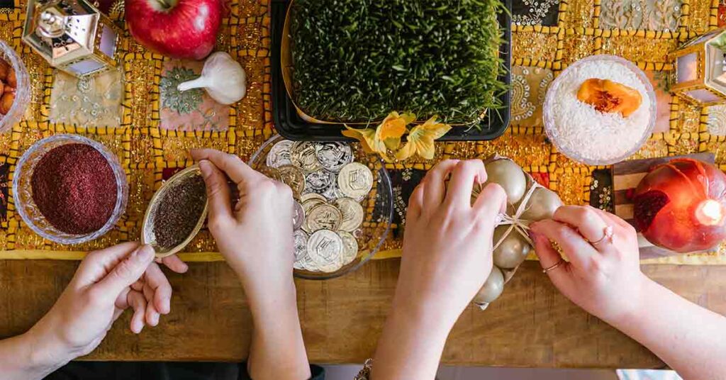 Two people prepare offerings of food, spices, candles, and coins to celebrate Nowruz.