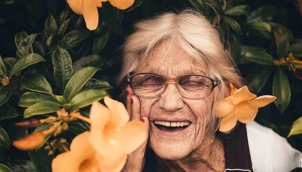 A smiling older woman standing by a bush with orange flowers