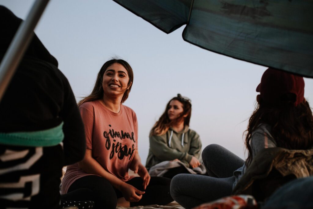 A group of bilingual friends smile together under an umbrella on the beach.