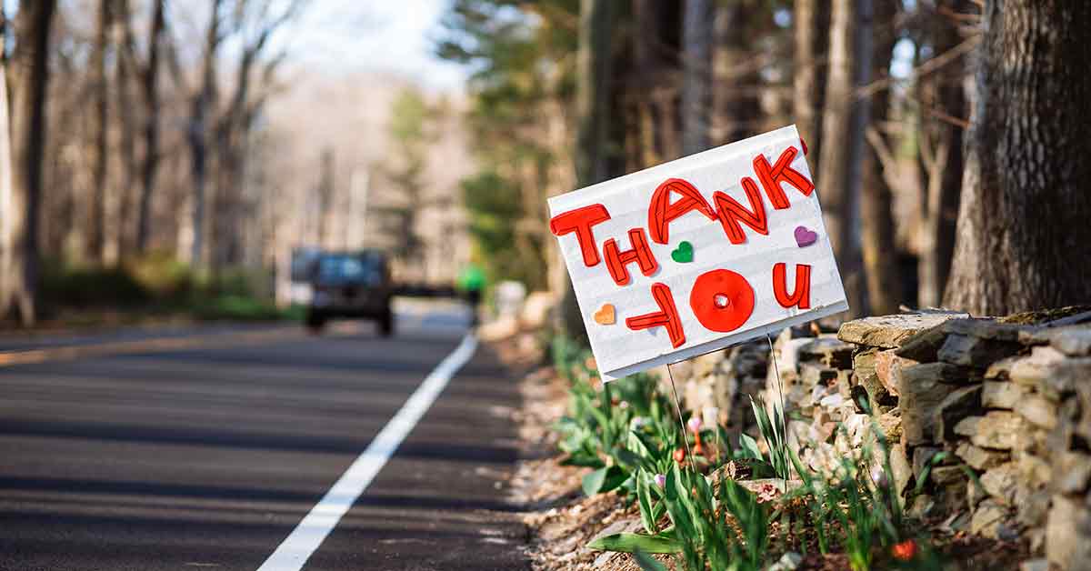 A hand-painted thank you sign with hearts stuck in the ground on the side of a road.