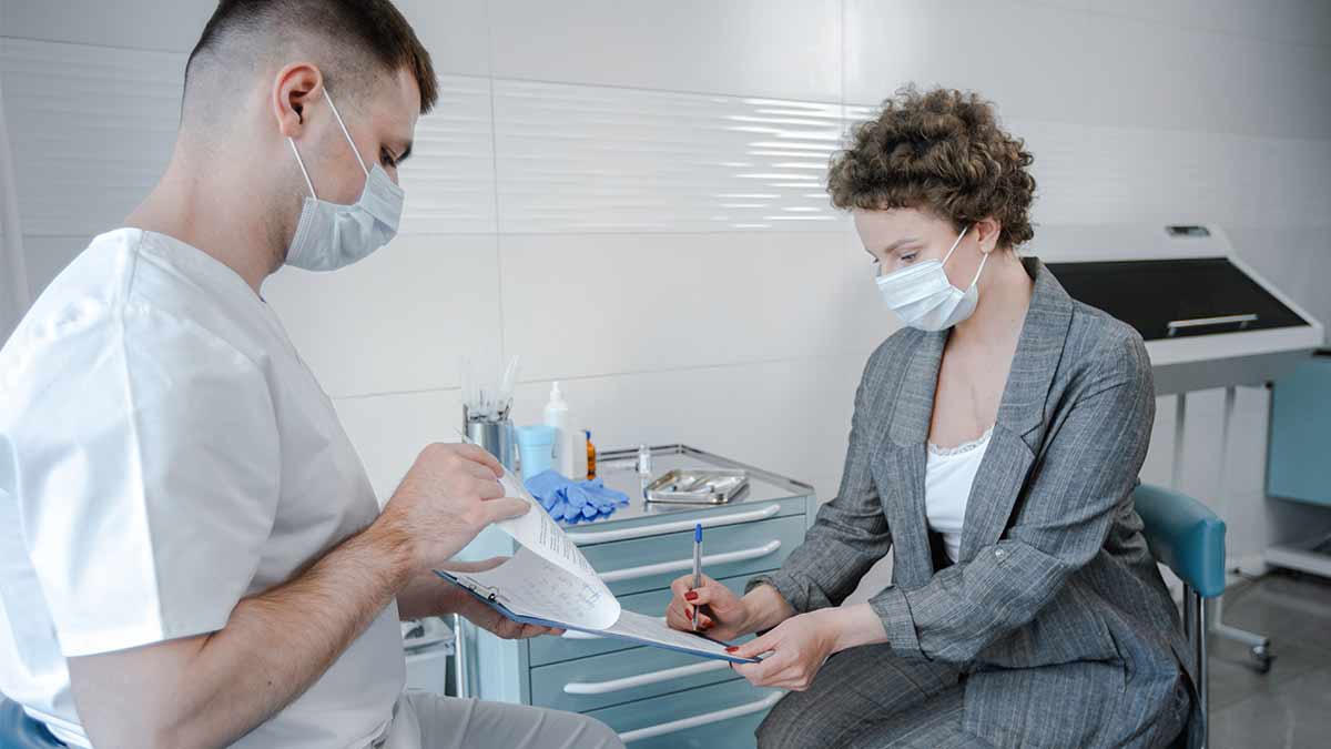 A doctor holds a translated document on a clipboard for a patient to sign.