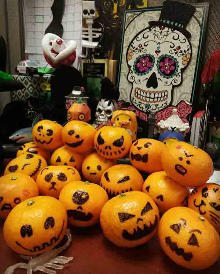 A pile of clementine fruit with drawn on jack-o'-lantern faces sit on Rochelle's decorated desk at CLI.