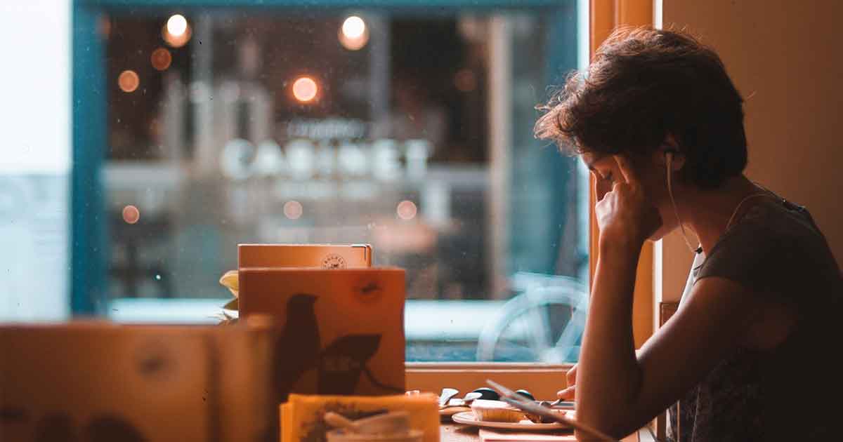 Woman with headphones sitting in a restaurant studying for her CMI certification