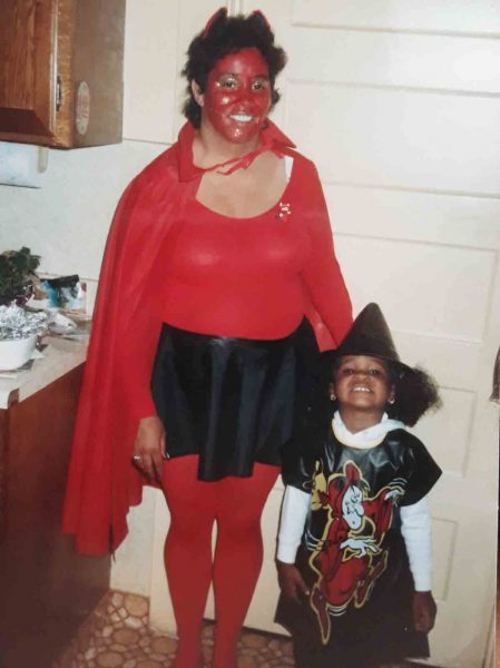 Little Rochelle dressed in a witches costume stands next to her aunt who's dressed as a red devil.