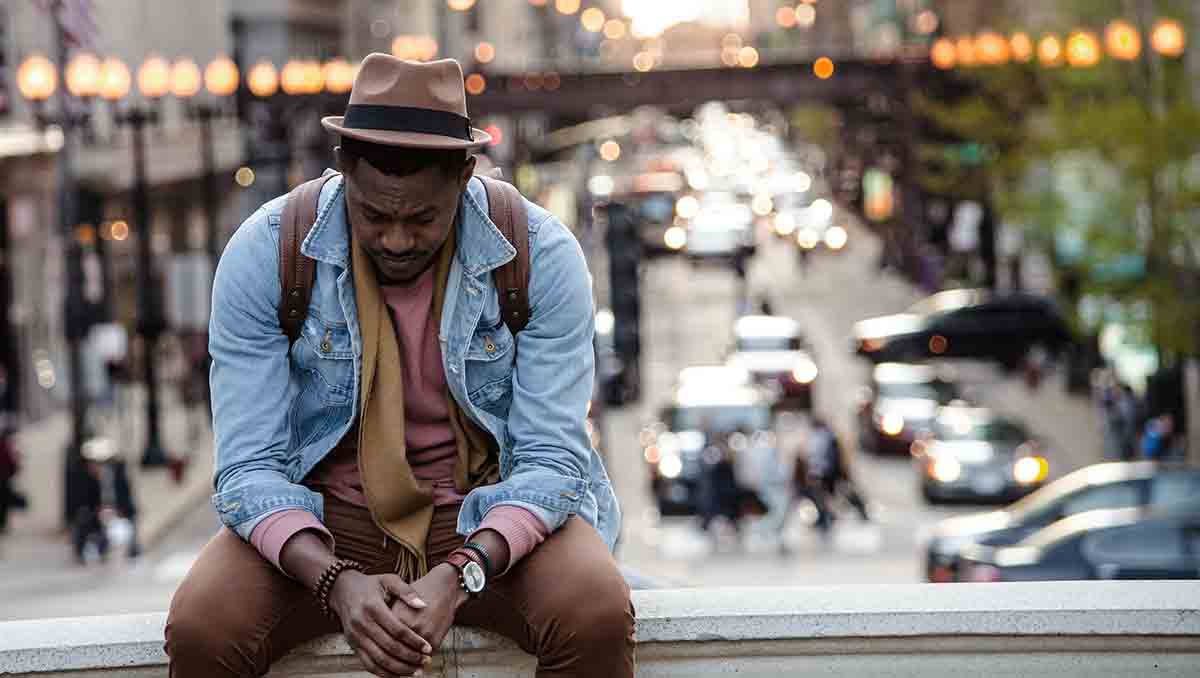 Male medical interpreter looking sad sitting on a ledge with his back to a cityscape.