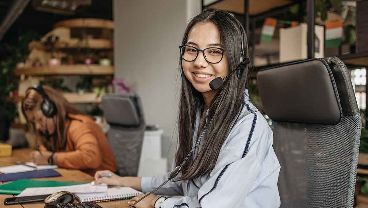 A female call center agent wearing a headset smiles while working in a call center during CMS call center monitoring.