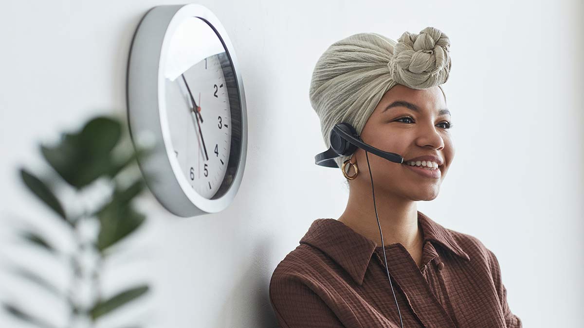 A remote interpreter wearing a headset smiles as they interpret for a deaf individual using a TTY device.