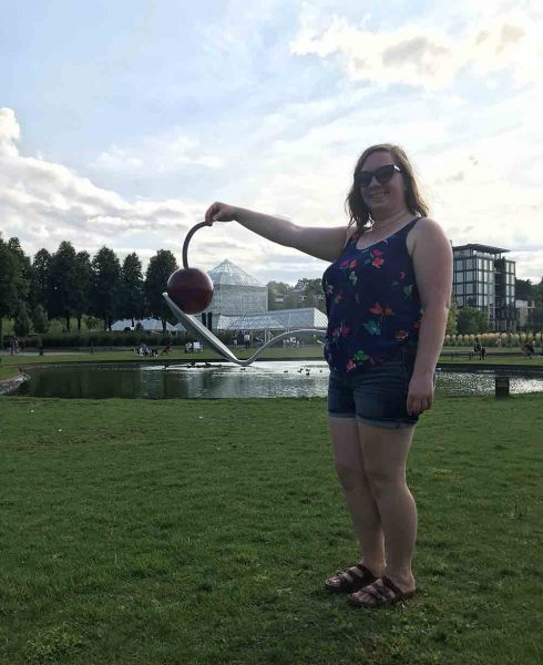 Corissa pretending to hold the stem of the Spoonbridge and Cherry fountain sculpture in Minneapolis.