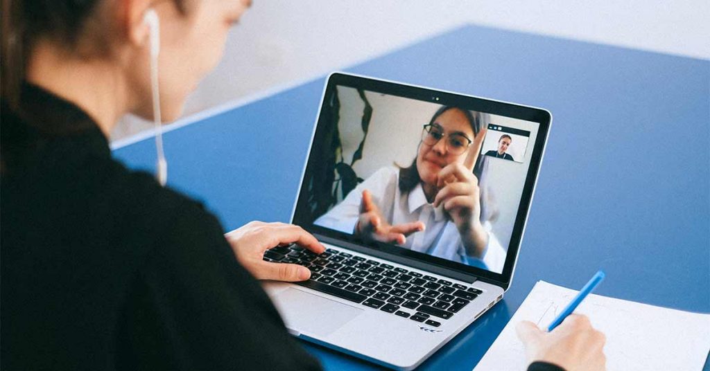 A banker holds a virtual meeting with a client through a laptop with the help of a video interpreter.