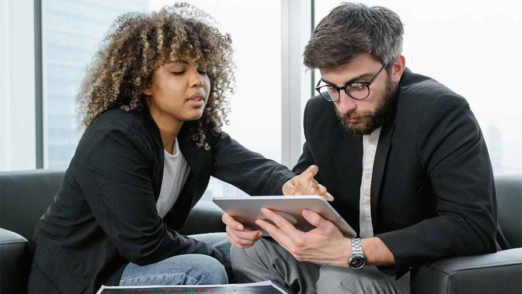 A loan officer explains terms to a client on a tablet.