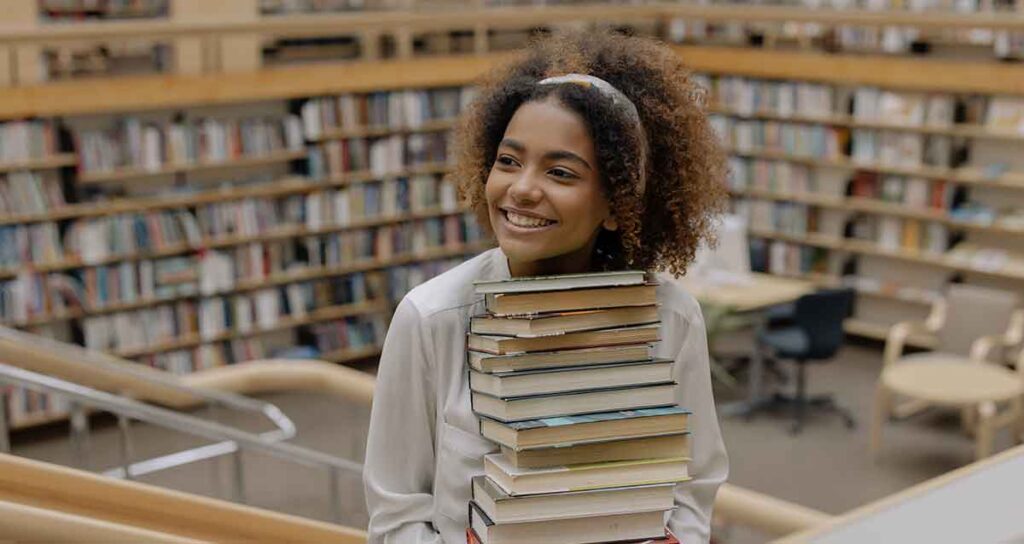 Smiling video interpreter carrying a stack of books up a staircase in the library.