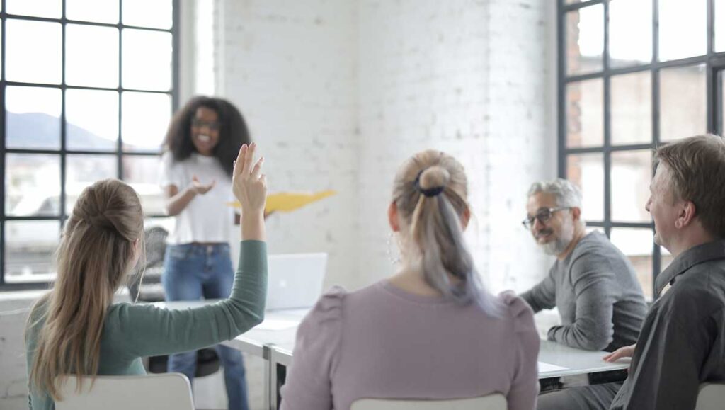 Four people watching a woman present on CMS call center monitoring. A woman raises her hand to ask a question.