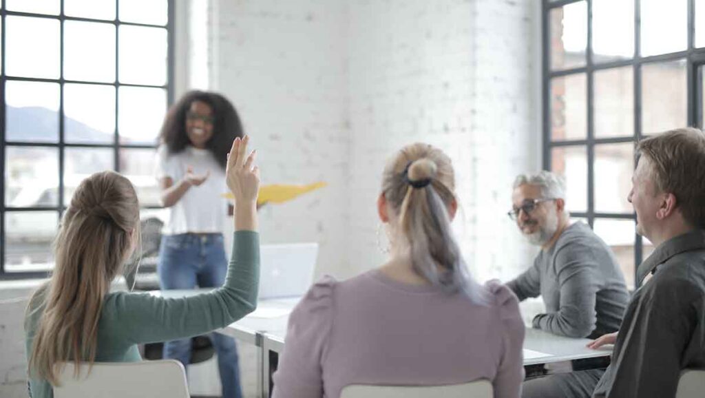 Four people watching a woman present on CMS call center monitoring. A woman raises her hand to ask a question.