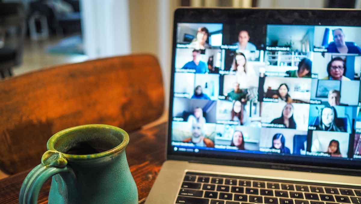 A coffee cup sitting next to a laptop with a Zoom meeting in progress. The computer screen displays several people in the video call.